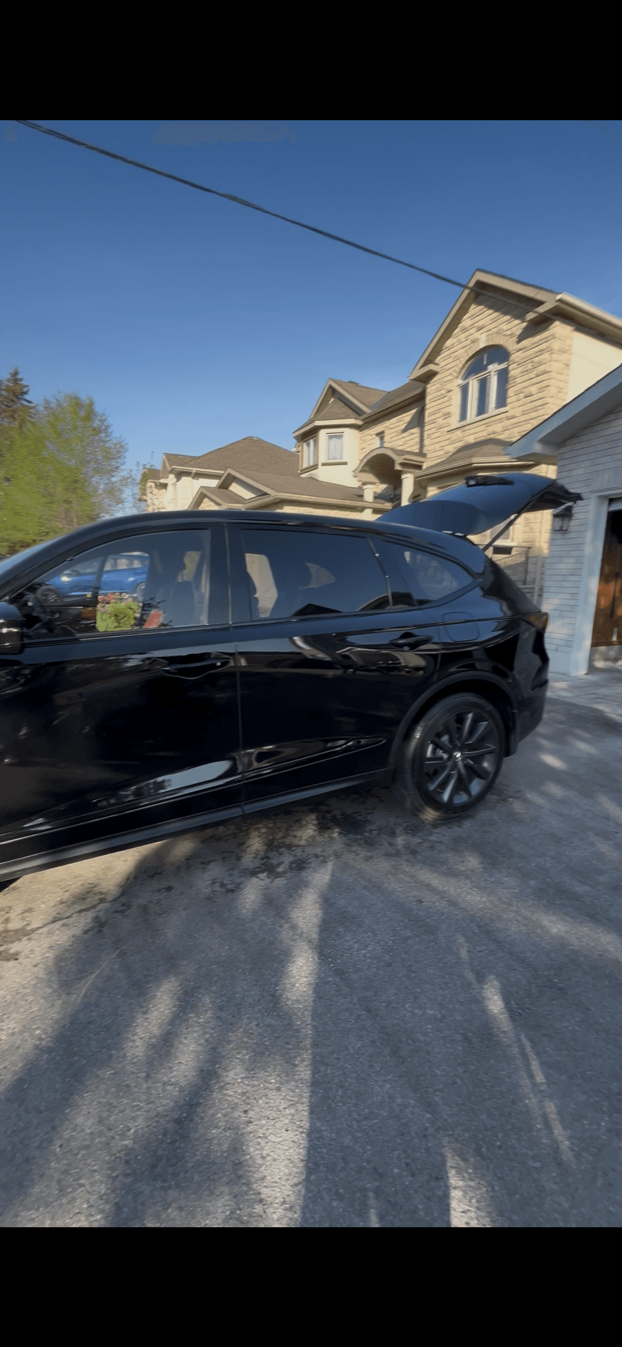 Black SUV with an open trunk parked in a driveway before a large stone house.
